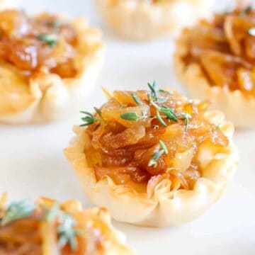 Several caramelized onion tartlets garnished with fresh thyme on a white platter.
