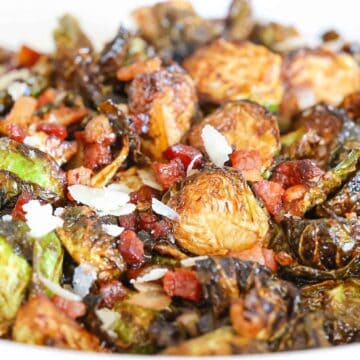 A white bowl filled with fried Brussels sprouts and crispy pancetta and garnished with freshly grated parmesan.