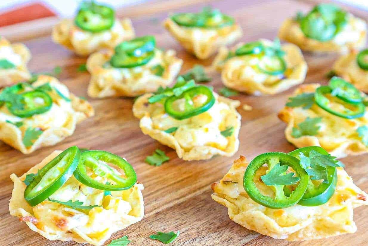 Tortilla chip scoops filled with cream cheese, pepper jack cheese, corn and jalapenos on a wooden serving board. 
