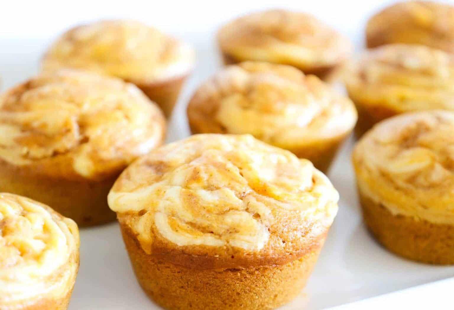 A close-up of freshly baked, golden-brown muffins with a creamy swirl topping on a white plate.