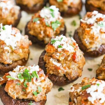 Several sausage stuffed mushrooms topped with freshly grated parmesan cheese and fresh parsley on a white plate.