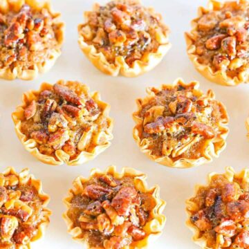 Several mini phyllo cup shells filled with pecan pie filling and baked on a white counter top.