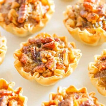 Several mini phyllo cup shells filled with pecan pie filling and baked on a white counter top.