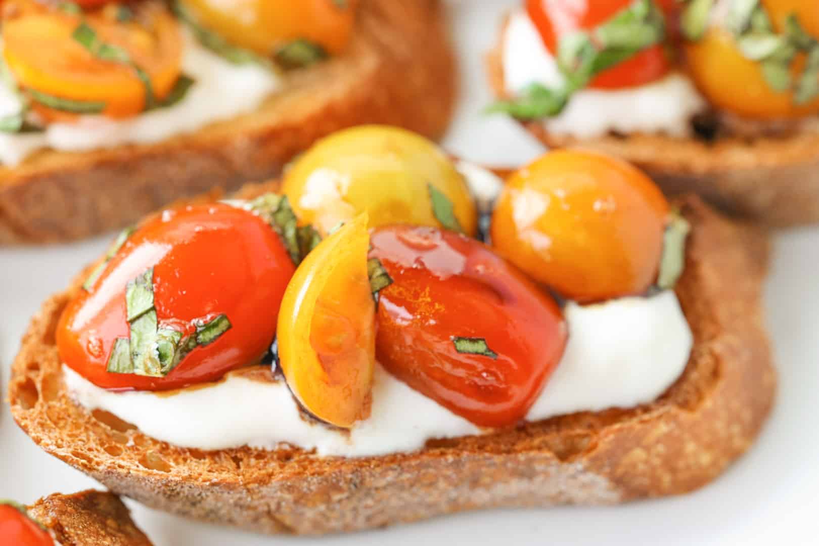 A piece of bruschetta topped with burrata cheese and caprese tomatoes, fresh basil and balsamic glaze.
