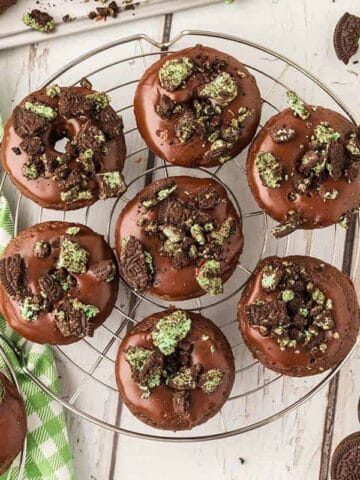 Nine mini chocolate cake mix donuts dipped a chocolate glaze and topped with crumbled mint Oreos on a wire rack.