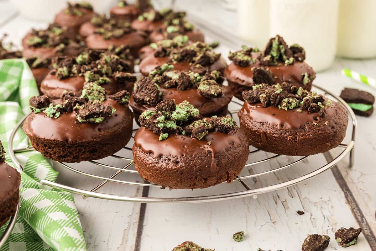 A picture of several mini chocolate cake mix donuts topped with mint Oreos on a wire rack.
