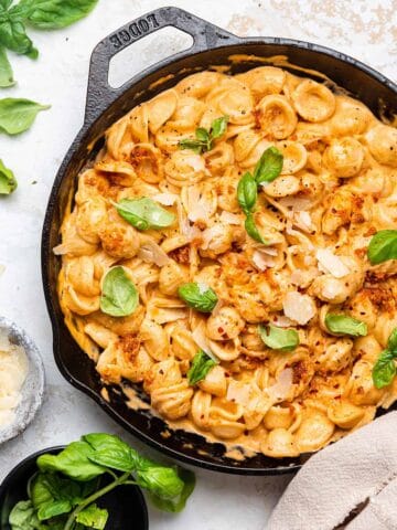 A large pan with a creamy sun dried tomato pesto sauce mixed with orecchiette pasta garnished with fresh basil leaves on a white counter top.