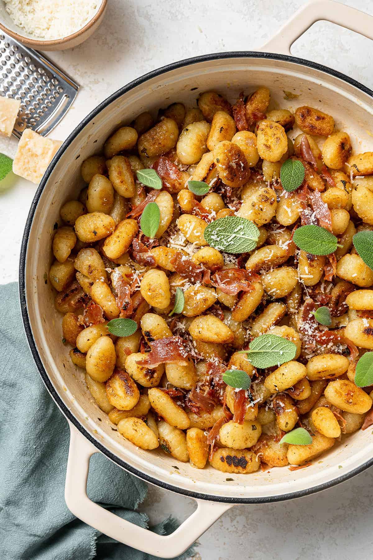 A large pot of lemon butter gnocchi with crispy prosciutto garnished with freshly grated parmesan cheese and fresh sage leaves.