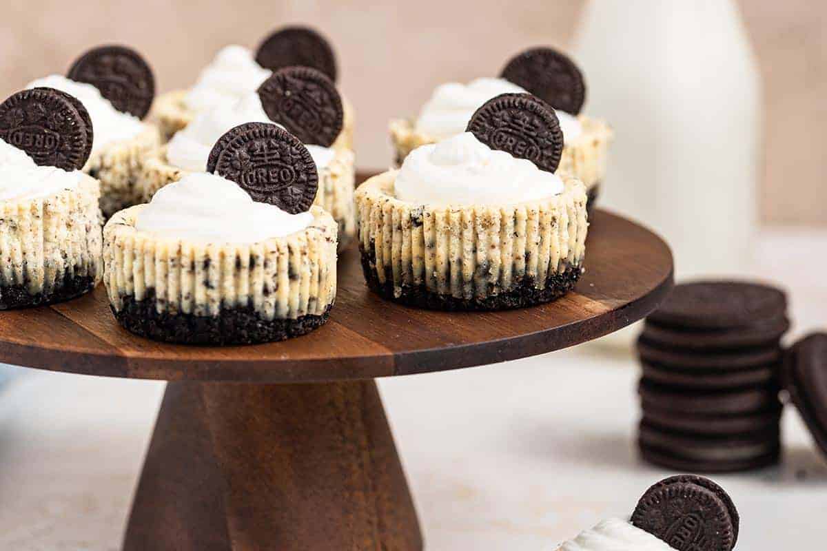 Seven Oreo Cheesecake Bites topped with whipped cream and a mini oreo on a wooden cake stand.