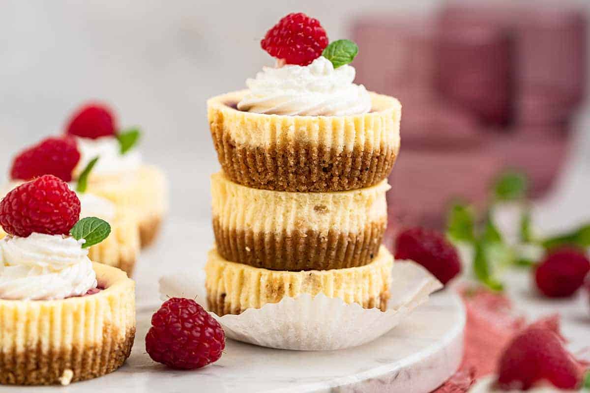Three mini cheesecakes stacked on top of each other on a white dessert plate.