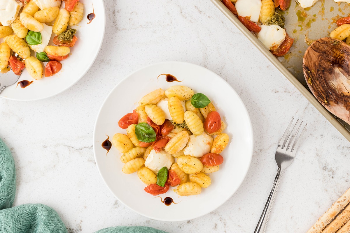 Two bowls of caprese gnocchi sheet pan dinner on two white plates on a white counter top.