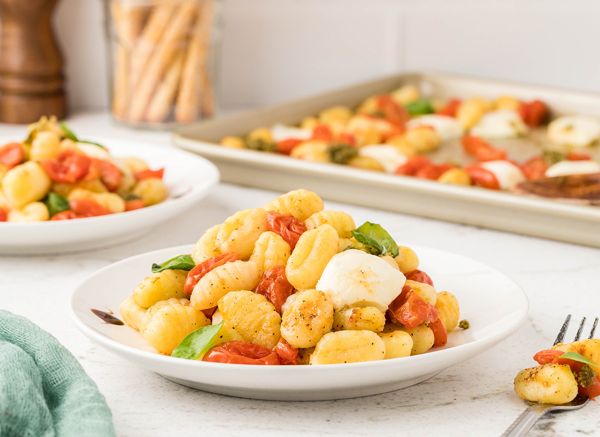 Two white bowls with sheet pan caprese gnocchi and a jar of bread sticks in the background.