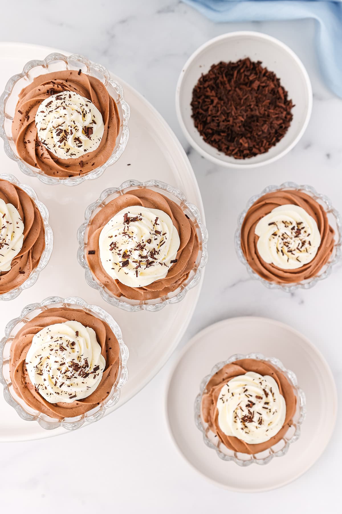 Six dessert glasses filled with Nutella chocolate cheesecake mousse topped with homemade whipped cream and chocolate shavings on a white counter top.