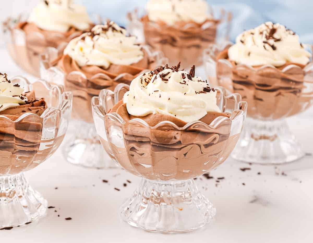 Six glass cup serving dishes filled with whipped Nutella chocolate cheesecake mousse topped with whipped cream and dark chocolate shavings.