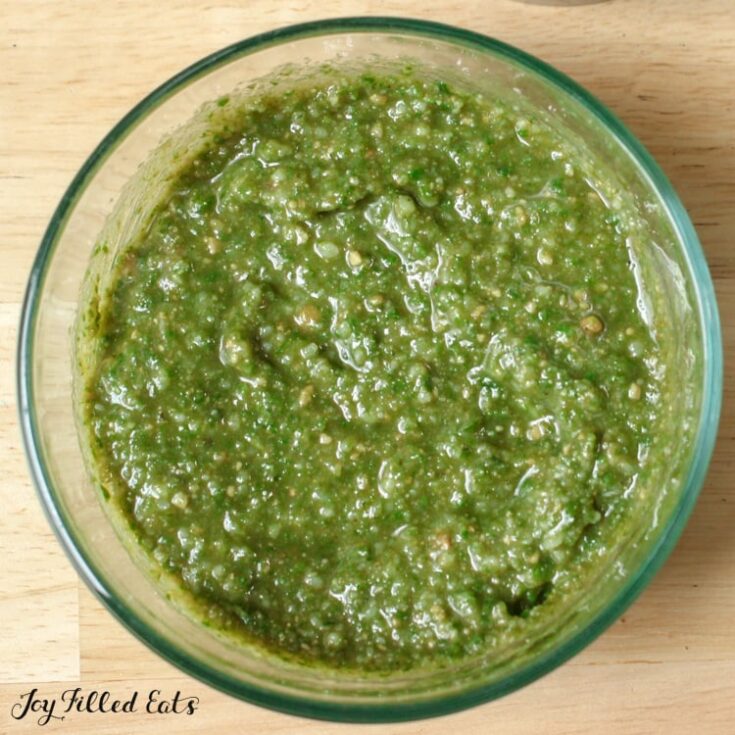 A large glass jar of nut free pesto on a wooden counter top.