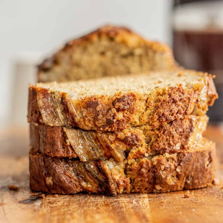 Three pieces of brown butter banana bread stacked on top of each other on a wooden cutting board.