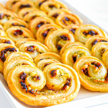 Several palmiers leaning against each other on a white serving platter on a white counter.