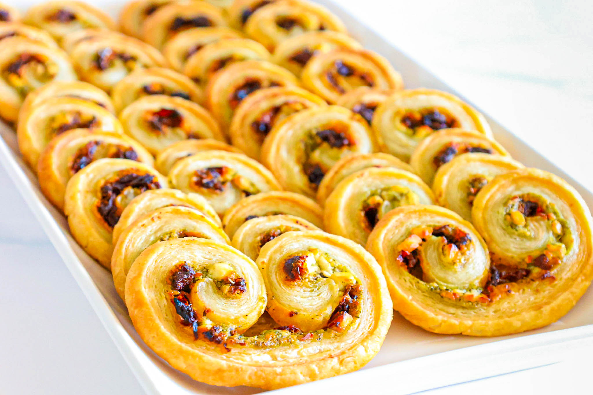 Several palmiers leaning against each other on a white serving platter on a white counter.