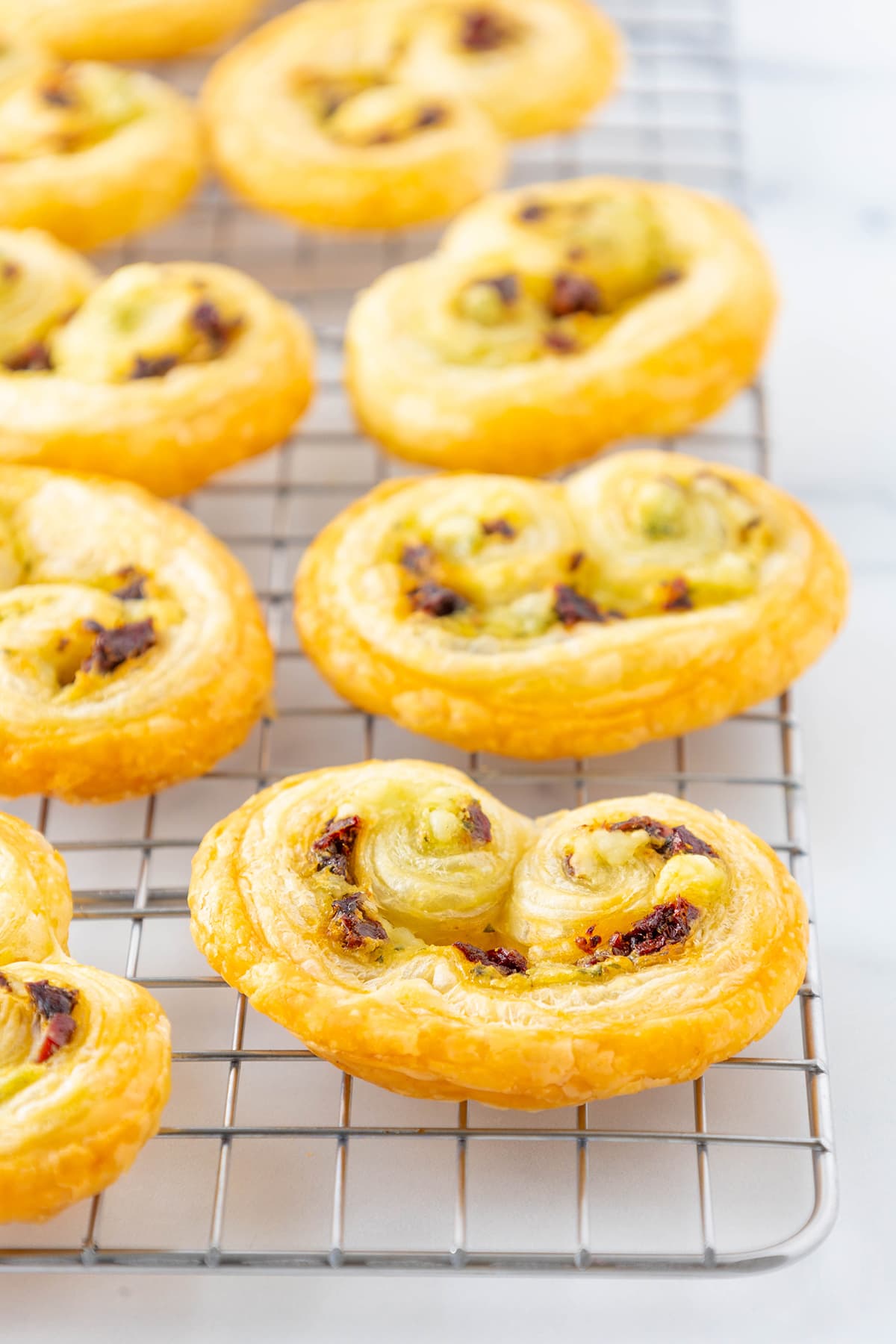 Several puff pastry palmiers laying on a silver cooling rack on a white counter top.