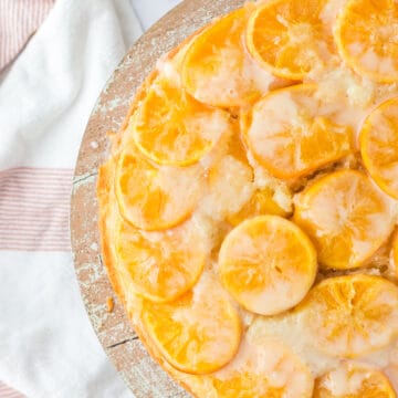 Half of an orange upside down cake on a wooden platter on a white counter top.