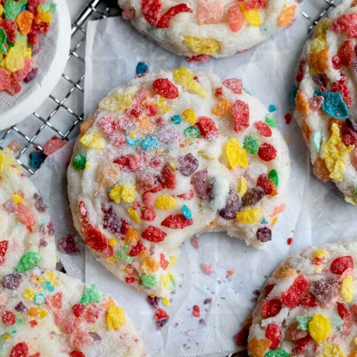 Several fruity pebbles cookies topped with white frosting and more fruity pebbles on white parchment paper.