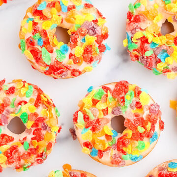 Nine baked, glazed, and topped fruity pebble donuts on a white counter top.