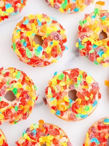 Nine baked, glazed, and topped fruity pebble donuts on a white counter top.