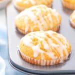 A six cup muffin tin filled with glazed lemon muffins on a white counter top with a light blue napkin.