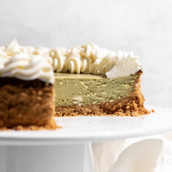 A matcha cheesecake with a slice missing on a white cake stand.