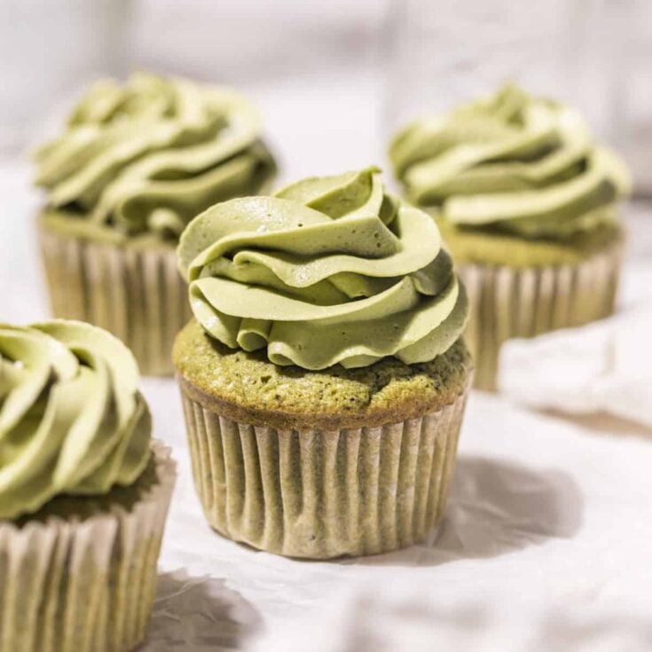 Four matcha cupcakes topped with matcha green tea frosting resting on white parchment paper.