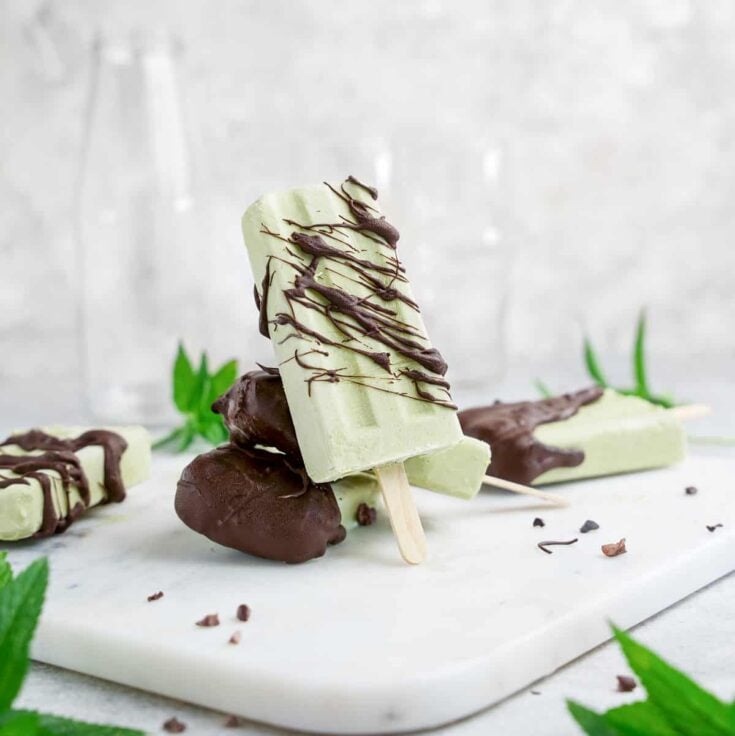 Three matcha mint chocolate chip popsicles resting on each other on a white serving board.