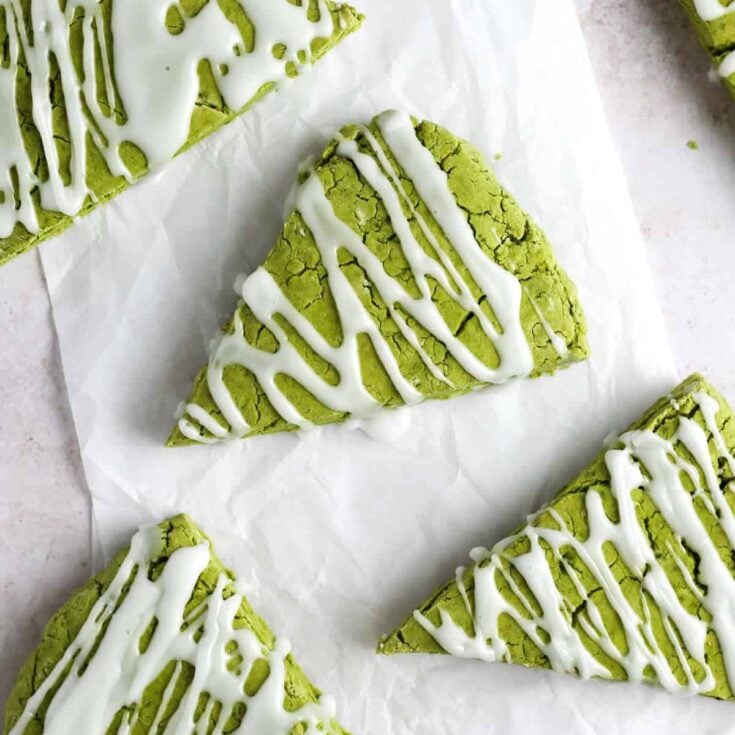 Four pieces of matcha scones drizzled with white icing resting on white parchment paper.