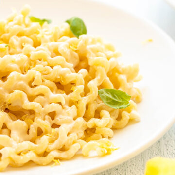 A large white bowl of long fusilli pasta with a lemon basil cream sauce on a white wooden counter top.