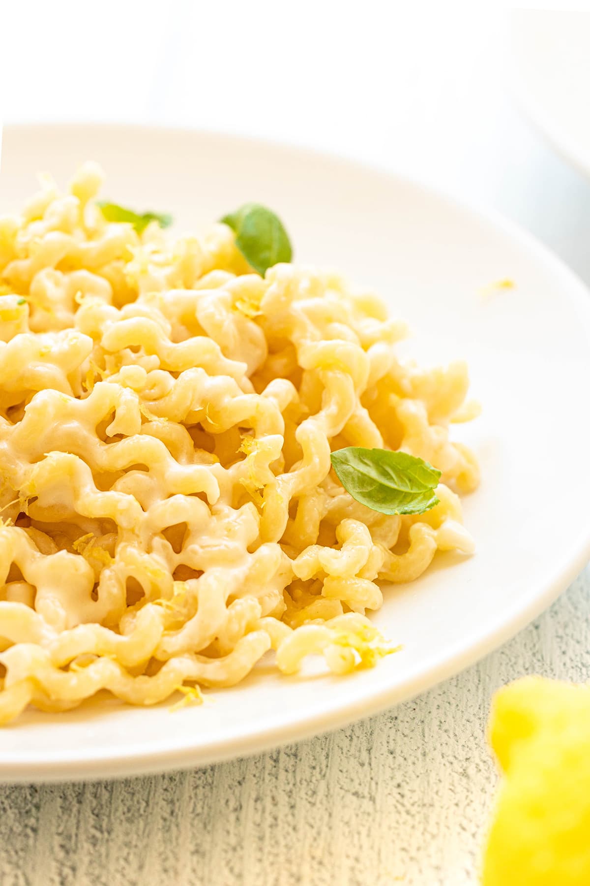 A large white bowl of long fusilli pasta with a lemon basil cream sauce on a white wooden counter top.