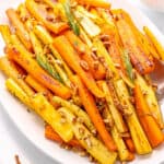 A large white platter with carrots and parsnips topped with fresh rosemary and chopped pecans on a white counter top.