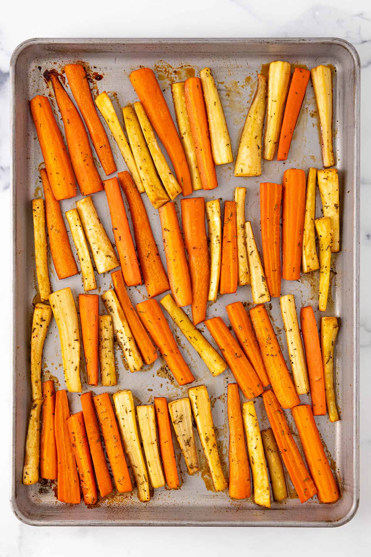 A large silver sheet pan with roasted parsnips and carrots.