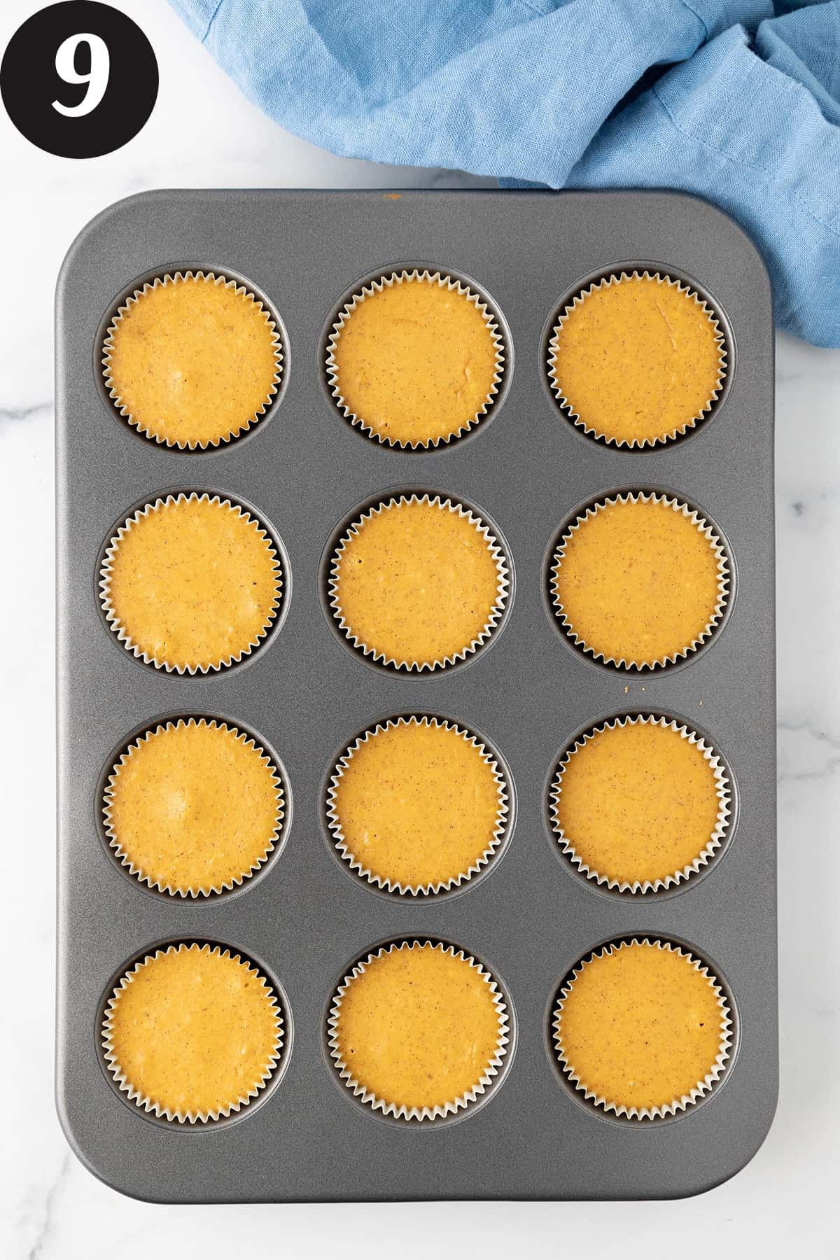 Twelve small pumpkin cheesecakes that have been cooked in a muffin pan resting on a white counter top.