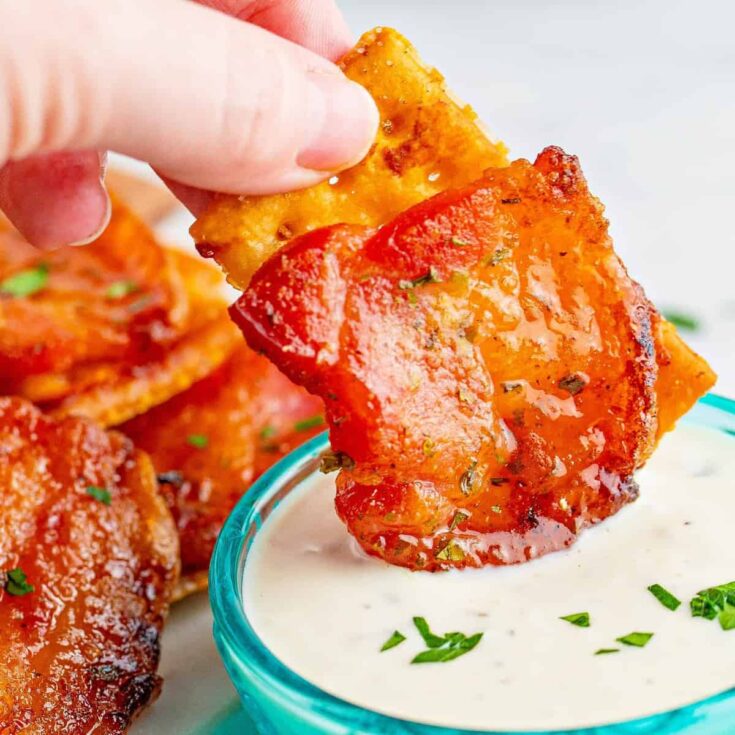 One piece of a bacon ranch cracker being dipped into ranch dressing.