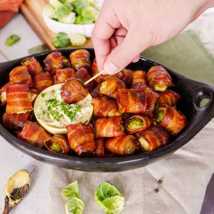 Brussels sprouts wrapped in bacon and baked in a large black serving bowl.