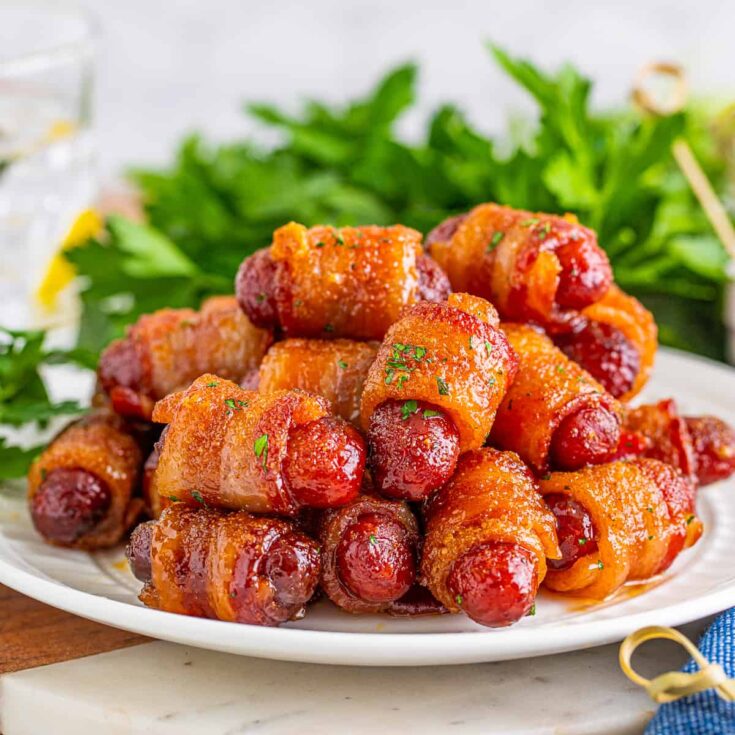 Several brown sugar bacon little smokies on a white serving platter with fresh parsley.