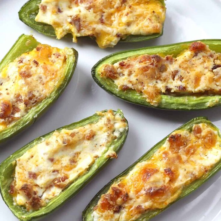 Five pieces of bacon jalapeño poppers on a white serving platter.