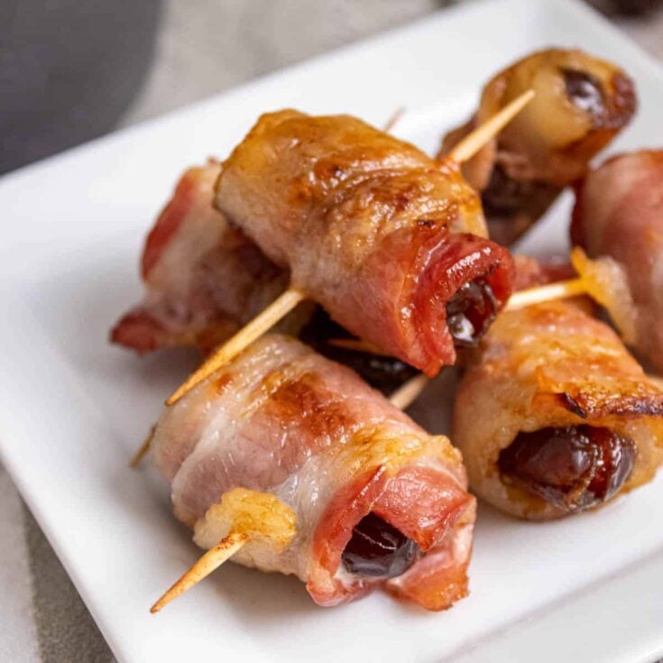 Several bacon wrapped dates on a white serving platter.