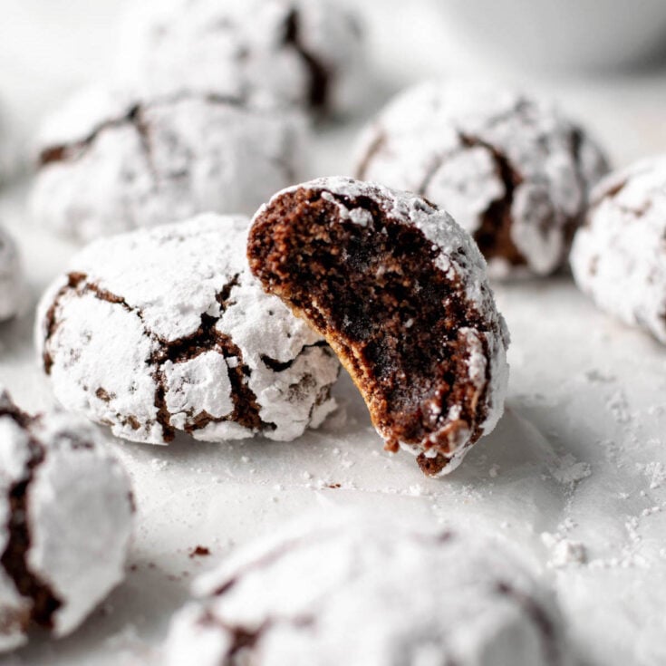 Several chocolate amaretti cookies on a white counter, one with a bite taken out of it leaning against another chocolate amaretti cookie.