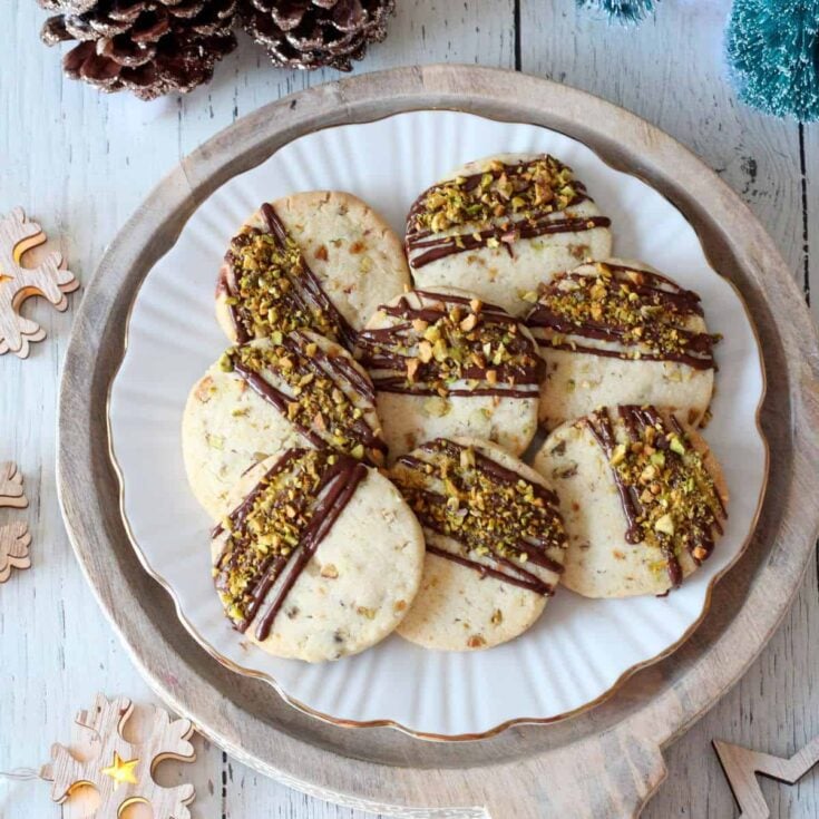 Eight Italian pistachio cookies on a white serving plate on a light wooden board.