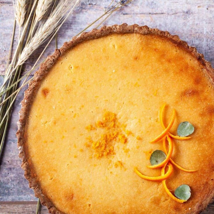 An italian ricotta tart topped with orange zest on a wooden counter.