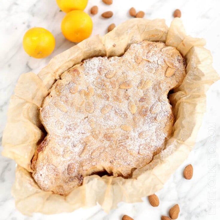 Italian easter dove bread dusted with powdered sugar on a white counter top with scattered almonds and whole fresh lemons.