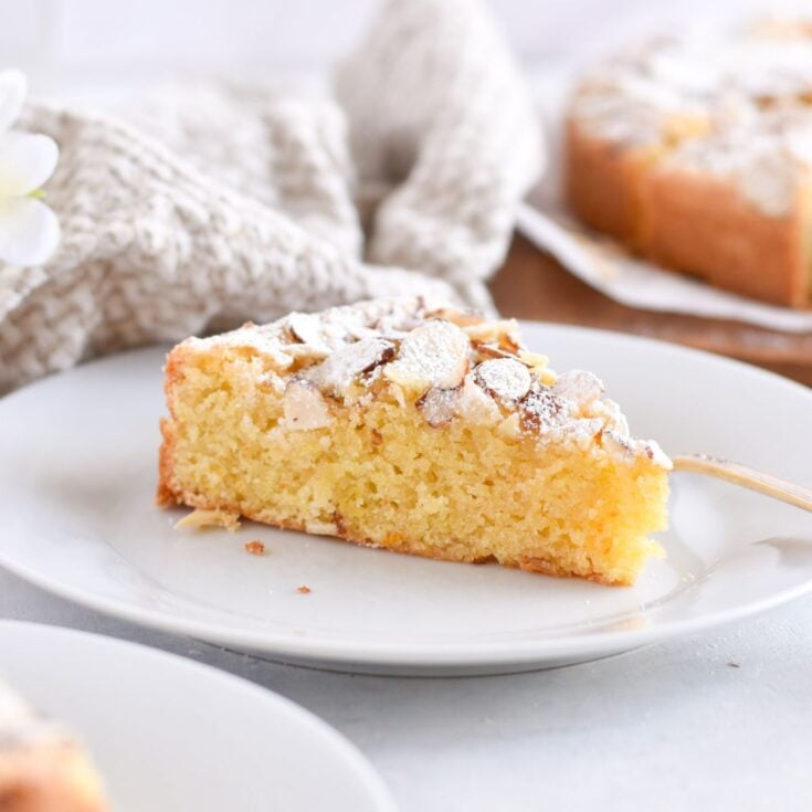 One slice of Italian almond cake on a white serving plate on a white counter.