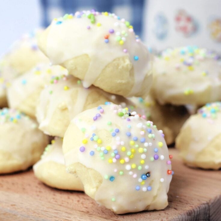 Several italian wedding cookies topped with pastel sprinkles piled on top of each other on a wooden serving board.
