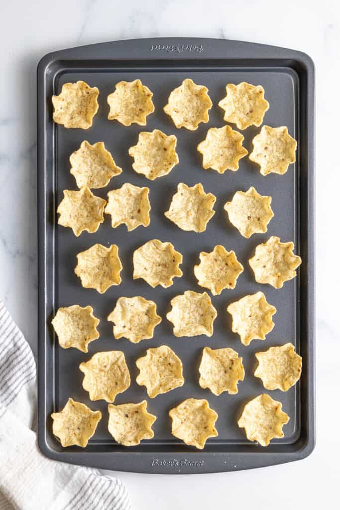 Several plain tostitos scoop chips on a large baking sheet on a white counter top.