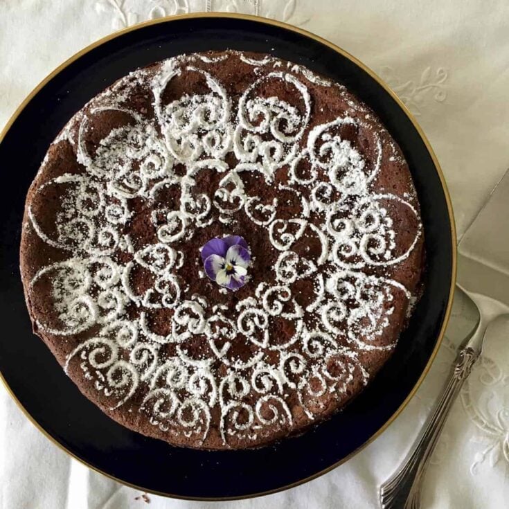 A large torta caprese cake sprinkled with powdered sugar on a dark serving platter.